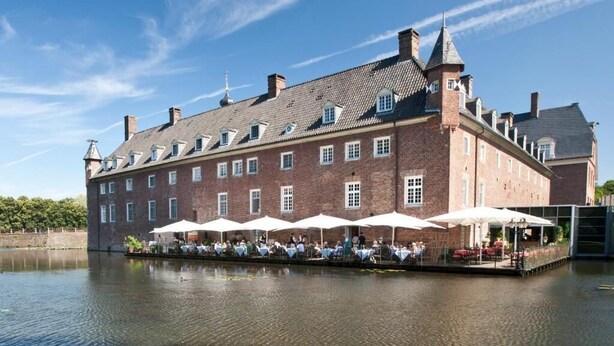 A historic brick building with a large courtyard and outdoor seating area. - Romantik Parkhotel Wasserburg Anholt (Isselburg)