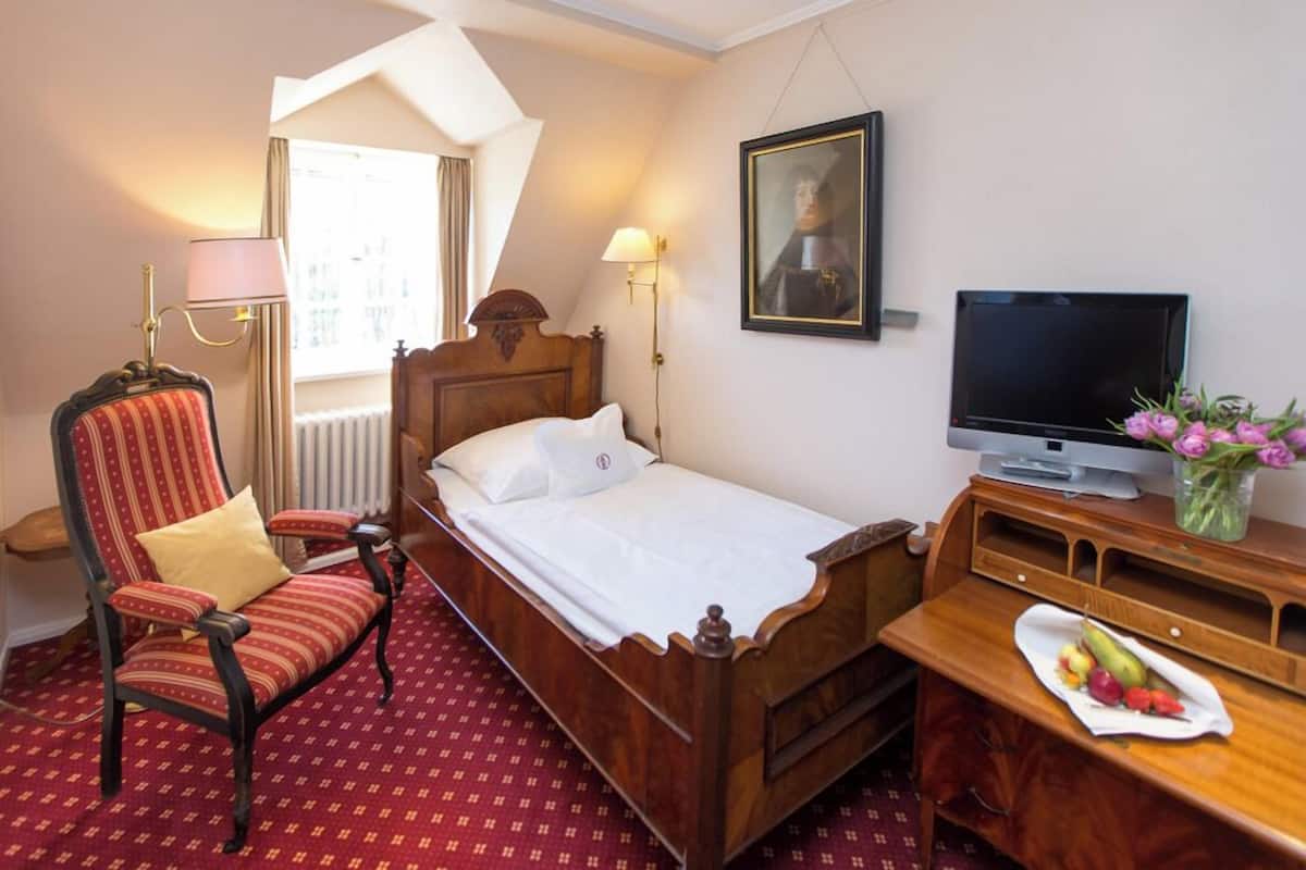 Ein Hotelzimmer mit Bett, Stuhl, Schreibtisch, Fernseher und einem Bild an der Wand.