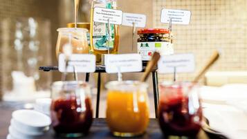 Buffet com diversos alimentos e acompanhamentos, incluindo potes de molhos e uma garrafa de xarope.