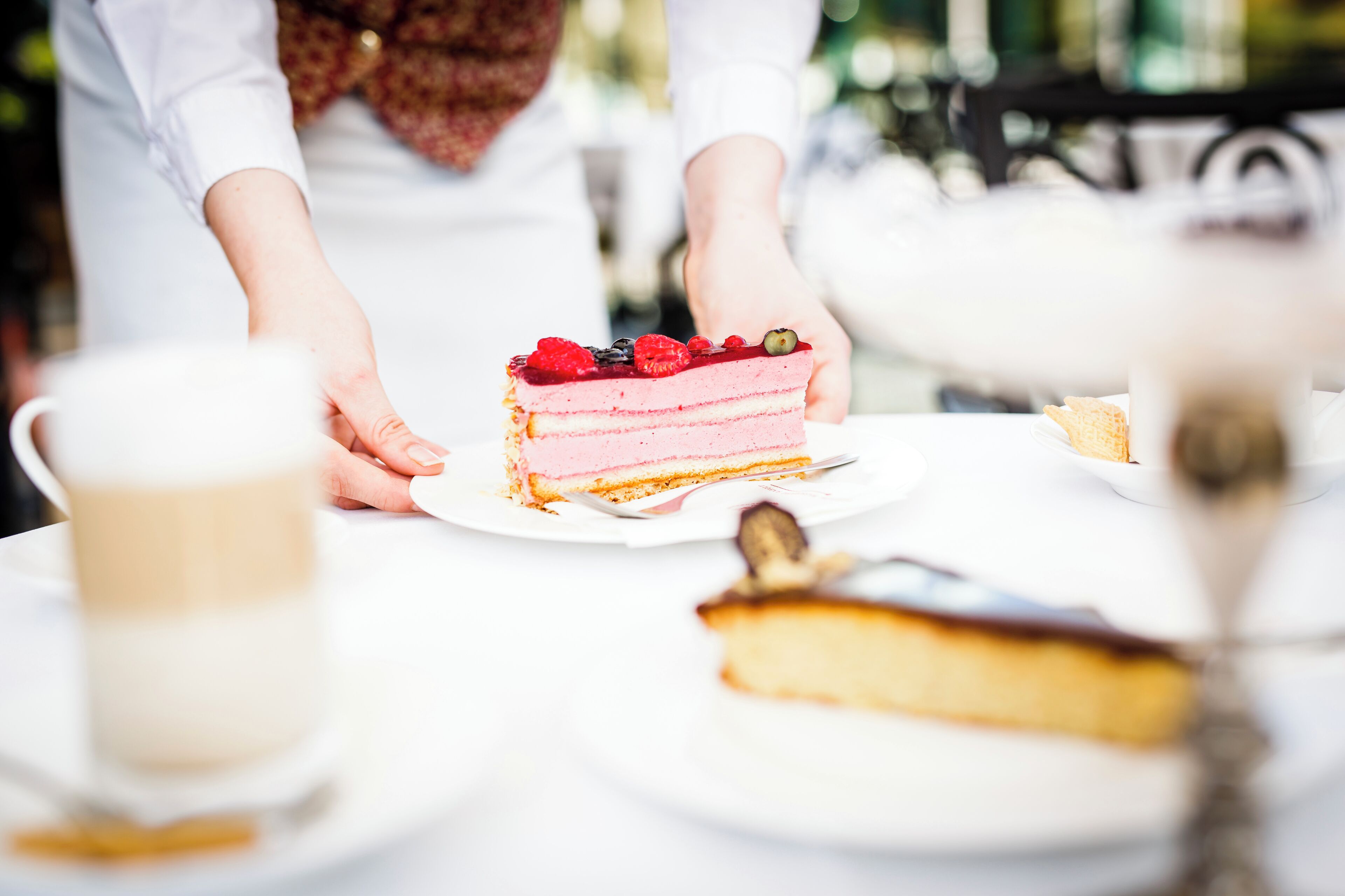 A slice of layered cake on a plate, a cup of coffee, and a tea cup on a table.
