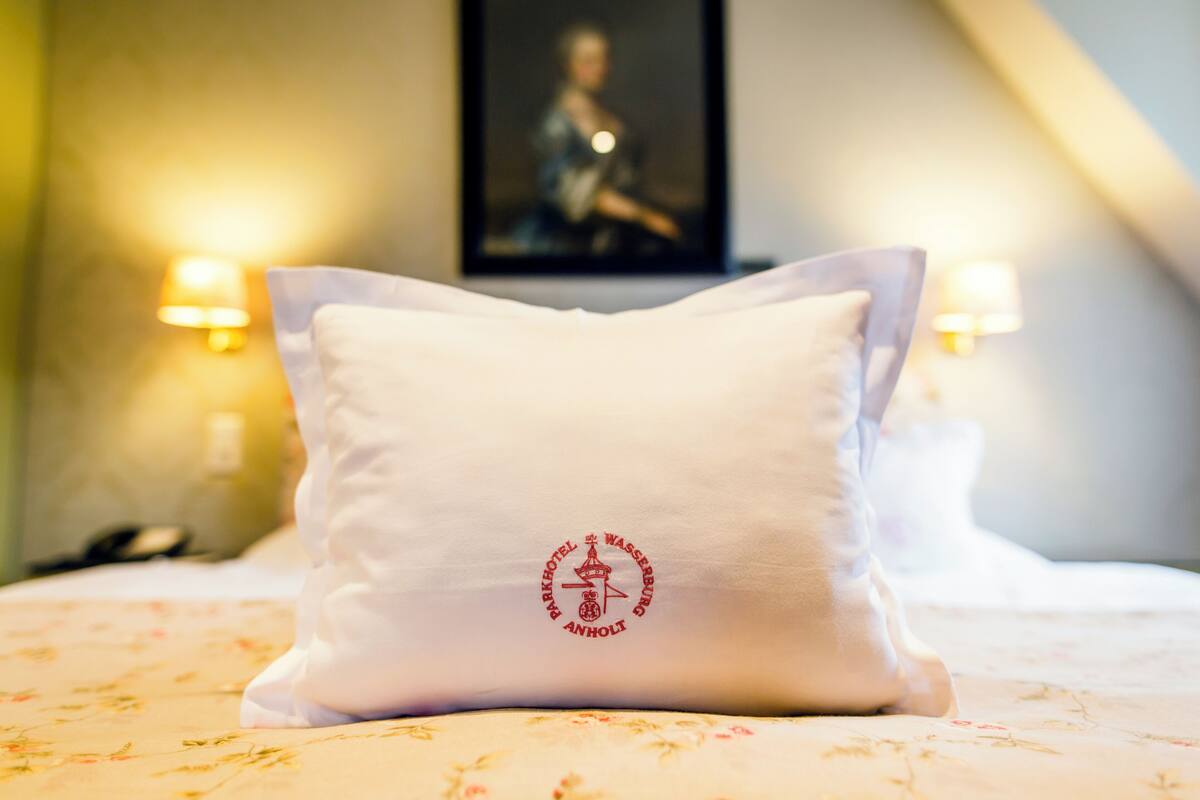 Ein Hotelzimmer mit einem Bett, einem Kopfkissen mit einem Logo und zwei Wandlampen.
