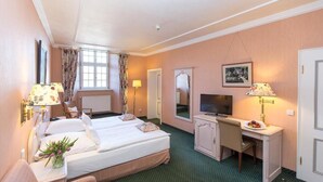 A hotel room with two beds, a desk, a television, and a mirror. - Romantik Parkhotel Wasserburg Anholt (Isselburg)