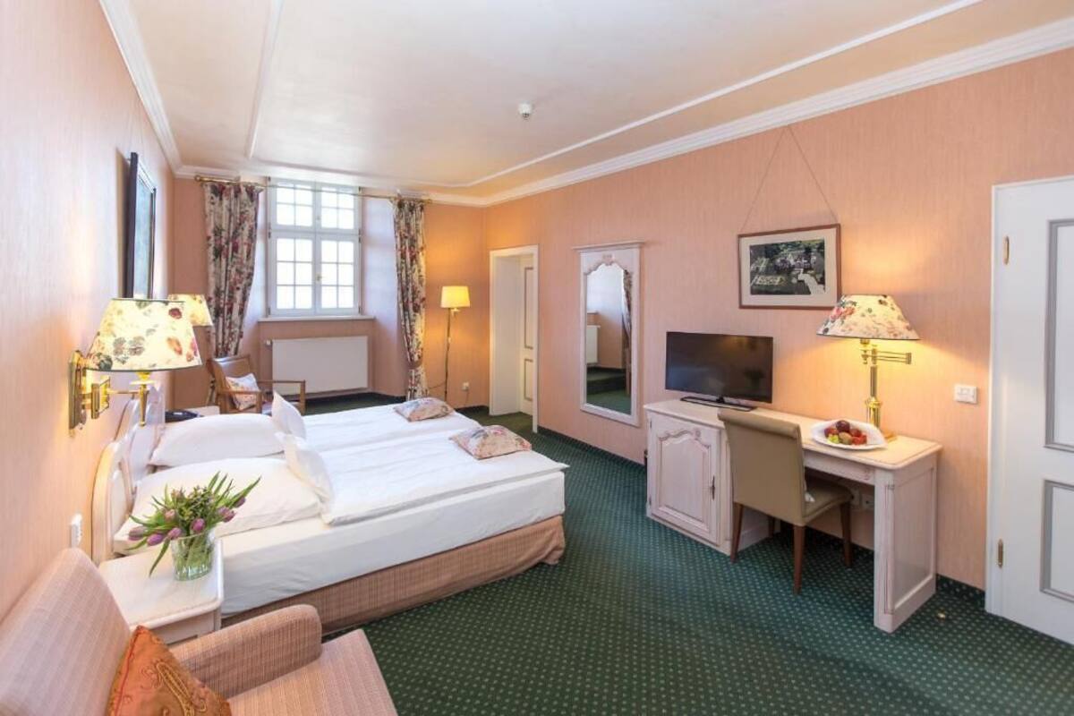 Ein Hotelzimmer mit zwei Betten, einem Schreibtisch, einem Fernseher und einem Spiegel.