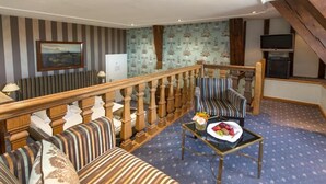 A hotel room with a balcony, striped upholstered sofas, a small table with fruit, and a television on a stand. - Romantik Parkhotel Wasserburg Anholt (Isselburg)