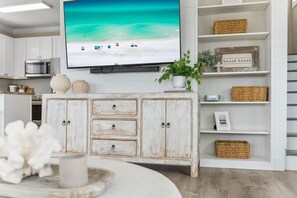 A kitchen with white cabinets, a white cabinet with drawers, a television mounted on the wall, and a shelf with wicker baskets and a sign that reads "beach house". - Luxury Gulf View Retreat on 30A, Steps to Sand, Sleeps 15, Pool, Golf Cart, Pets (Santa Rosa Beach)