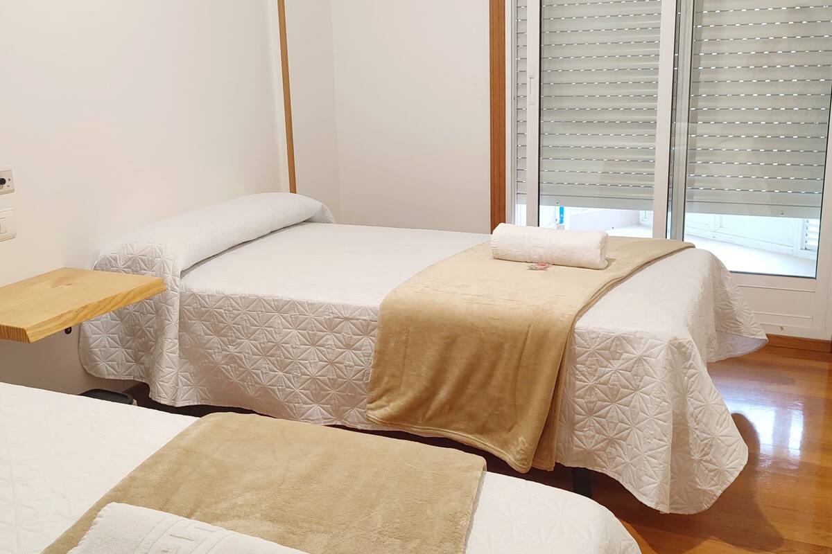 Camera d'albergo con due letti, un comodino in legno, una finestra con tende e un pavimento in legno.
