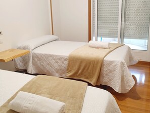 A hotel room with two beds, a wooden shelf, and a window with blinds.