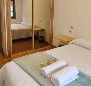 A bedroom with a bed, a wooden wardrobe, a small table, and a mirror.