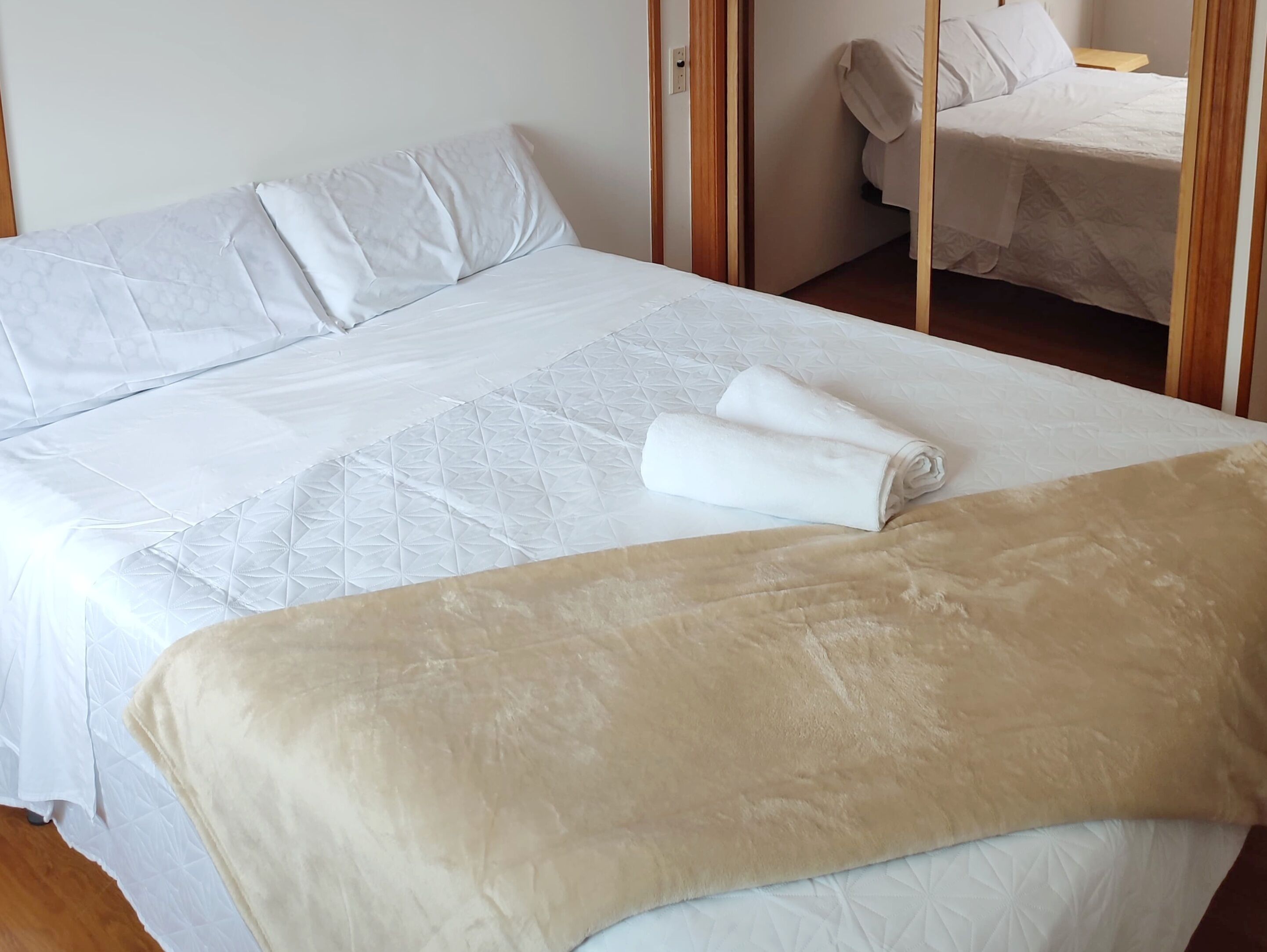 Een net opgemaakt bed met een witte dekbedovertrek en een beige plaid.