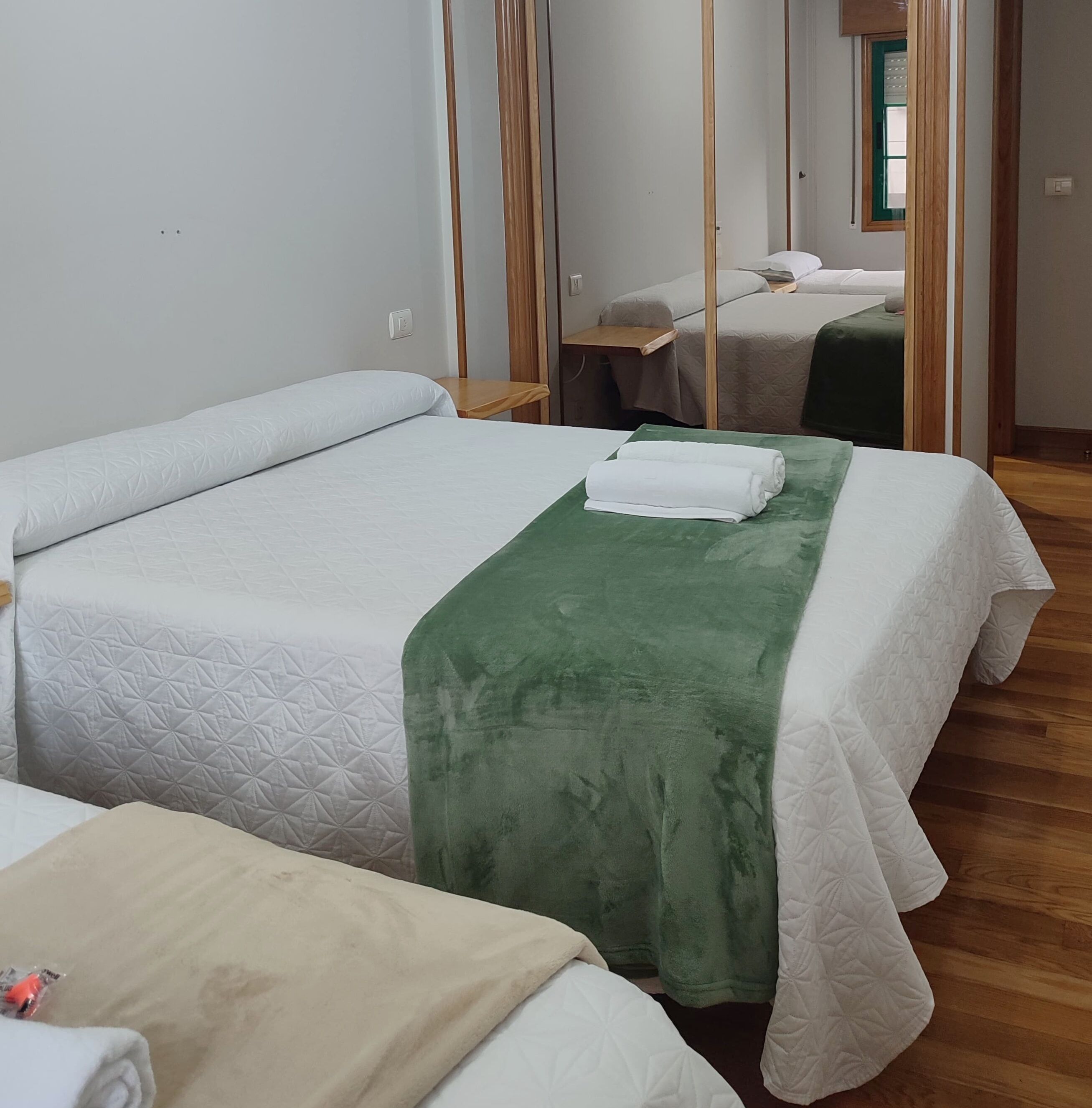 A hotel room with two beds, a wooden floor, and a mirror reflecting the room.