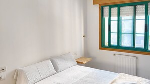 Un dormitorio con una cama, una ventana con persianas, una mesita de noche y un radiador.