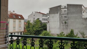 A balcony with a wrought iron railing, a hanging lantern, and a view of residential buildings in the background. - Pensión Armonía (Caldas de Reis)