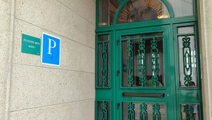 A green metal gate with a 'P' parking sign, a 'Peluquería Mixta Manoli' sign, and a building entrance with a green awning. - Pensión Armonía (Caldas de Reis)