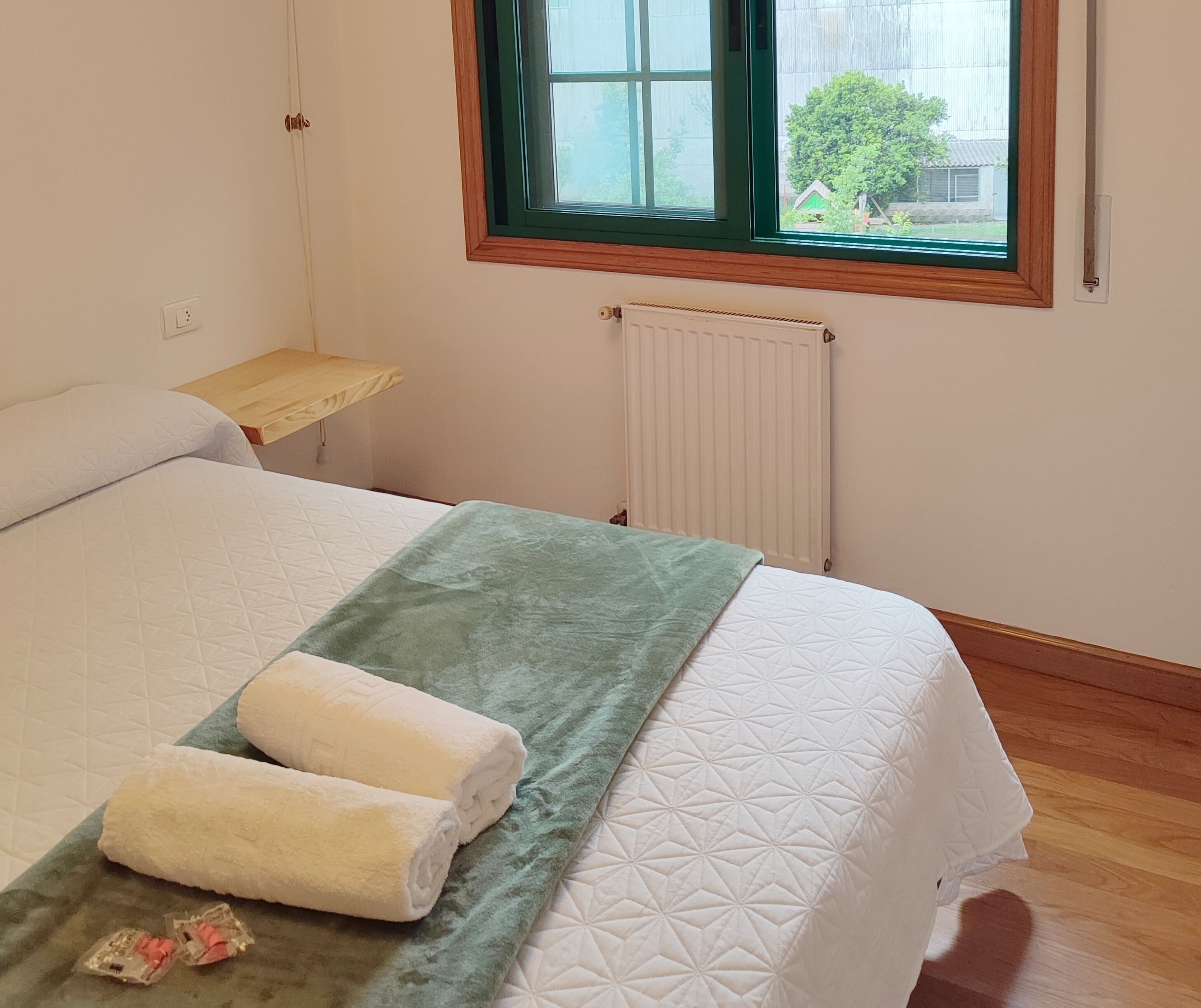 A bedroom with a bed, a window, a radiator, and a wooden nightstand.