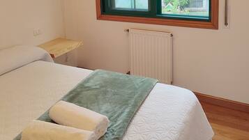 A bedroom with a bed, a window, a radiator, and a wooden nightstand.