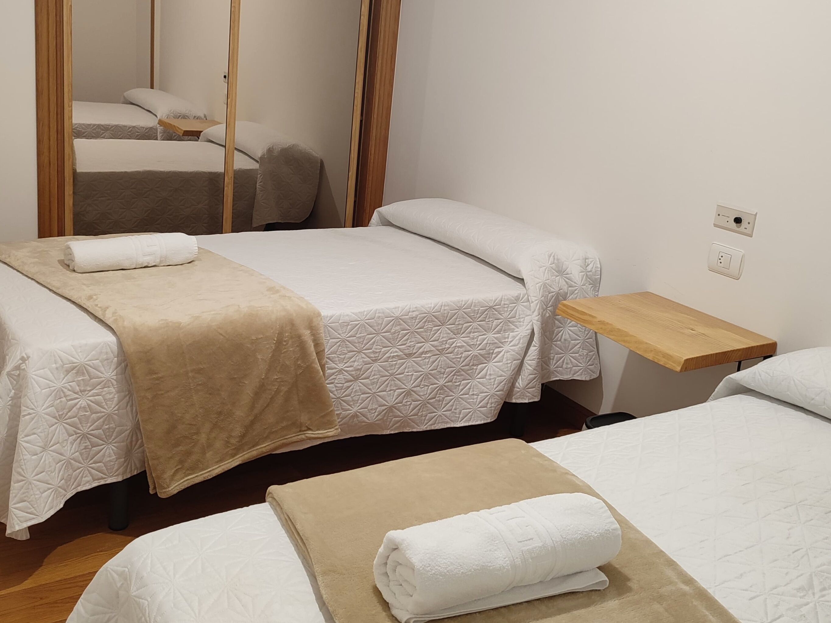 A hotel room with two beds, a wooden nightstand, and a mirror.