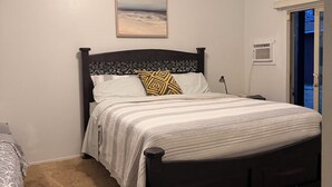 A bedroom with a bed, a ceiling fan, a window, and a wall-mounted air conditioner.