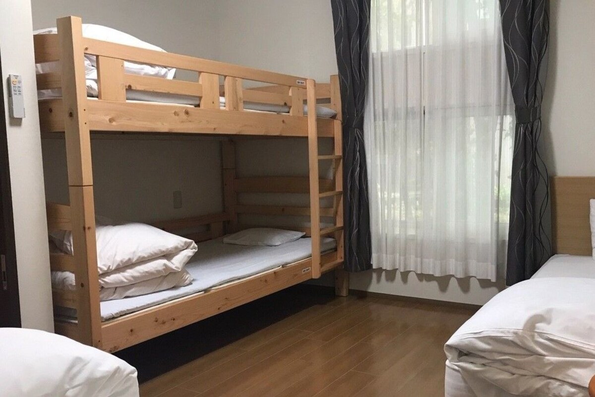 A room with a bunk bed, a single bed, a bedside table, and a lamp.