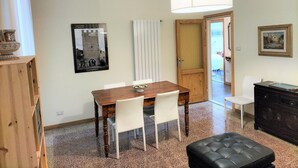 A dining area with a wooden table, white chairs, a black cushioned bench, a hanging light fixture, a framed picture, and a door leading to another room. - Giannotti Vintage Apartment With Two Bedrooms (Firenze)