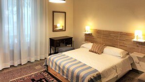 A hotel room with a bed, bedside lamps, a desk, a mirror, and a hanging light fixture. - Giannotti Vintage Apartment With Two Bedrooms (Firenze)
