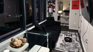 Ett modernt vardagsrum med ett soffbord i glas, en svart soffa och en mönstrad matta.