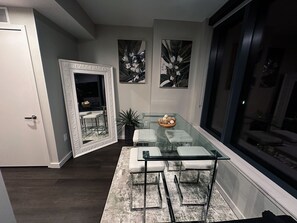 A modern dining area with a glass table and chairs, a decorative mirror, and two wall-mounted flower paintings. - Luxury High Rise • Rooftop Pool (Atlanta)
