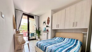 Ein Schlafzimmer mit einem Bett, einem Schreibtisch und einem Stuhl. Ein Schiebeglastür führt zu einem Außenbereich.