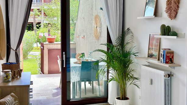 Ein Zimmer mit einer Schiebetür zum Außenbereich, einem Blumentopf, einem Tisch mit Stühlen und einem Heizkörper.
