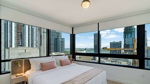 A modern bedroom with a large bed, a nightstand, and a view of city buildings through large windows. - Sky Corner Residence- Pool, Parking, Amenities (Miami)
