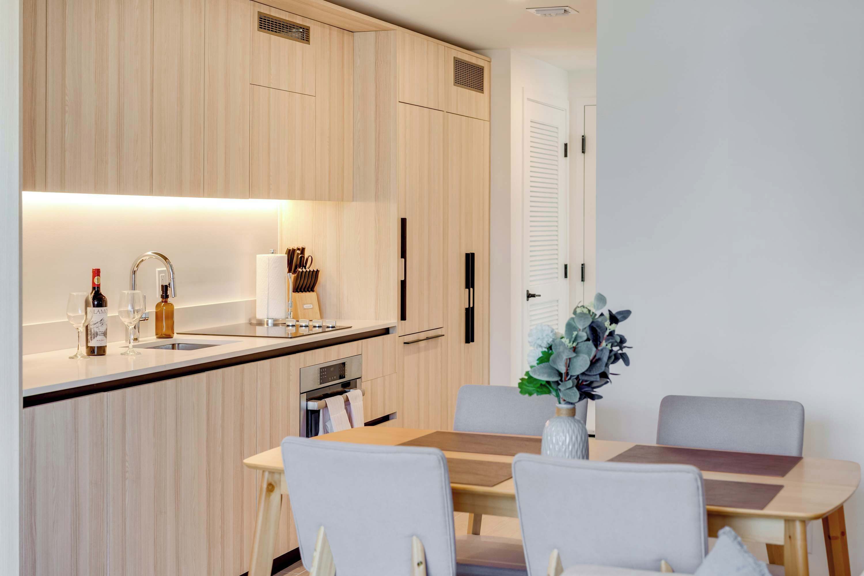 A modern kitchen with wooden cabinets, a built-in oven, and a dining area with a table and chairs.