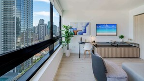 A modern living room with a large window, a dining area, and a view of the cityscape. - Sky Corner Residence- Pool, Parking, Amenities (Miami)