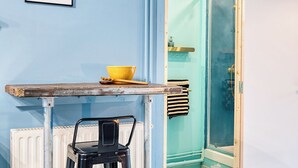 A small kitchenette with a stool, a bowl, and framed pictures on the wall. - Suite Privée, Bain, Kitchenette, en Champagne. (Orges)