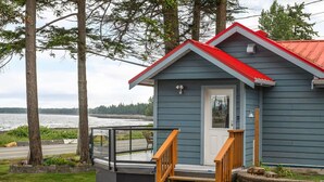 A small blue cabin with a red roof, a wooden staircase, and a glass railing overlooking a body of water. - Beachfront 2 bed | Arcade, A+ Views, Lux King bed (Strathcona D (Oyster Bay-Bu*)