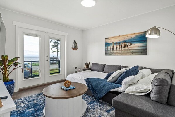 A modern living room with a grey sofa, a round coffee table, and a large window offering a view of the outdoors.