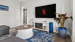 A modern living room with a fireplace, a television mounted on the wall, a round coffee table, and a potted plant. - Beachfront 2 bed | Arcade, A+ Views, Lux King bed (Strathcona D (Oyster Bay-Bu*)