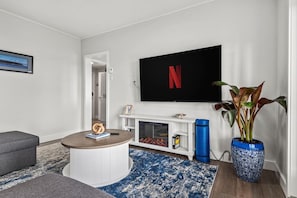 Una sala de estar moderna con chimenea, un televisor montado en la pared, una mesa de centro redonda y una planta en maceta.