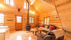 A log cabin interior with a fireplace, wooden floors, a sofa, and a dining table. - Uniquely landscaped log cabin with spa! (Lac-aux-Sables)