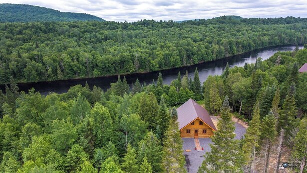 A cabin surrounded by dense forest and a river. - Uniquely landscaped log cabin with spa! (Lac-aux-Sables)