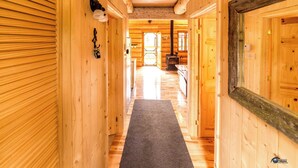 A wooden hallway with a central rug, wooden walls, and a large mirror on the right. - Uniquely landscaped log cabin with spa! (Lac-aux-Sables)
