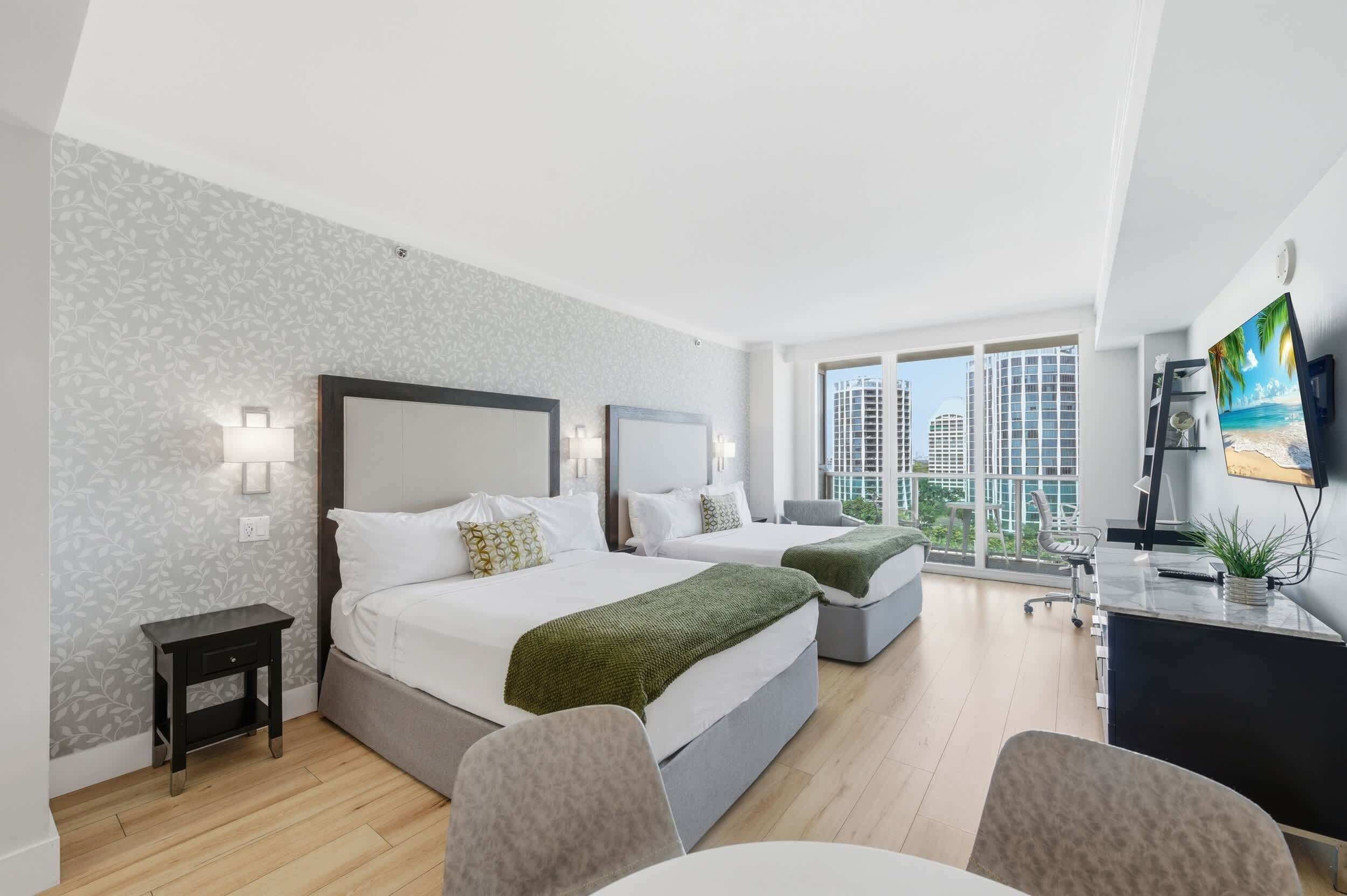Ein modernes Hotelzimmer mit zwei Betten, einem Schreibtisch und einem großen Fenster mit Blick auf die Stadt.