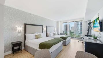 Ein modernes Hotelzimmer mit zwei Betten, einem Schreibtisch und einem großen Fenster mit Blick auf die Stadt.