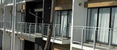 Een hotel met meerdere verdiepingen, balkons, een palmboom en een verzorgd gazon.