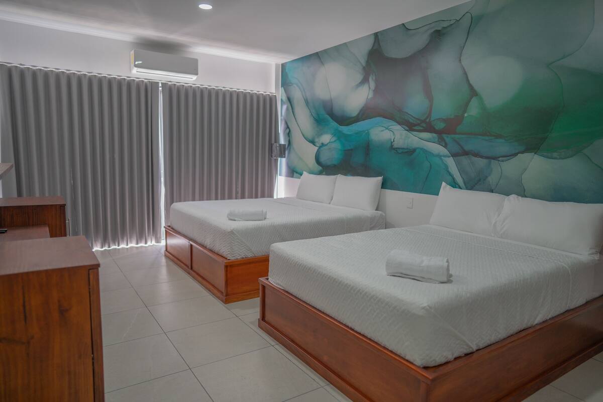 A hotel room with two beds, a wooden desk, and a large abstract mural on the wall.