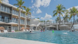 A swimming pool area with multiple levels of balconies, palm trees, and umbrellas. - Coco Blue Resort (La Libertad)