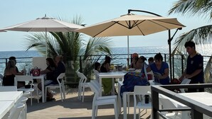 An outdoor dining area with white plastic chairs and tables, large umbrellas, and a view of the sea. - Coco Blue Resort (La Libertad)
