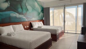 A hotel room with two beds, a large abstract mural on the wall, a sliding glass door to the balcony, and a dark wooden desk. - Coco Blue Resort (La Libertad)