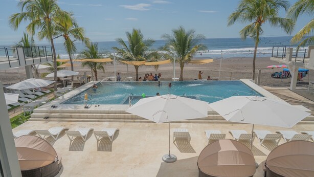 A pool area with lounge chairs, umbrellas, and a view of the beach. - Coco Blue Resort (La Libertad)