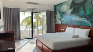 A hotel room with a large bed, a desk, and a view of palm trees through a sliding glass door. - Coco Blue Resort (La Libertad)