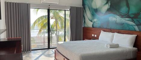 Habitación de hotel con una cama grande, un escritorio y vistas a palmeras a través de una puerta corrediza de vidrio.
