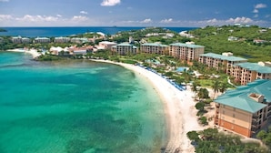 Luftaufnahme eines Küstenresorts mit Strandvillen, einem Sandstrand und klarem türkisblauem Wasser.